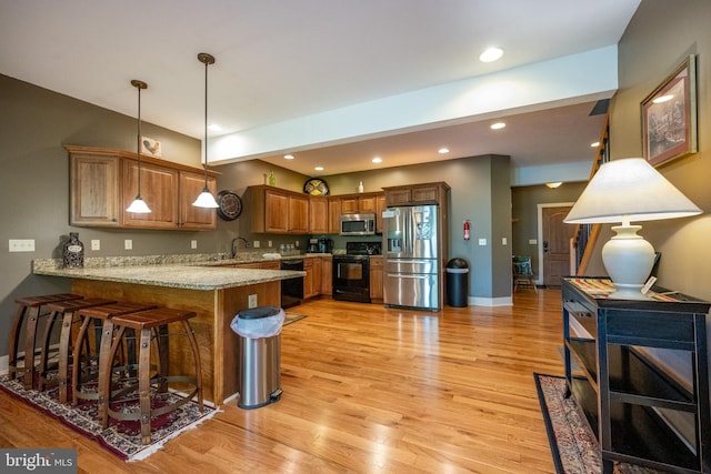 kitchen with light stone countertops, kitchen peninsula, decorative light fixtures, appliances with stainless steel finishes, and light hardwood / wood-style flooring