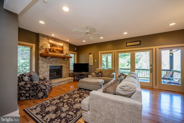 living room featuring a stone fireplace, ceiling fan, and hardwood / wood-style floors