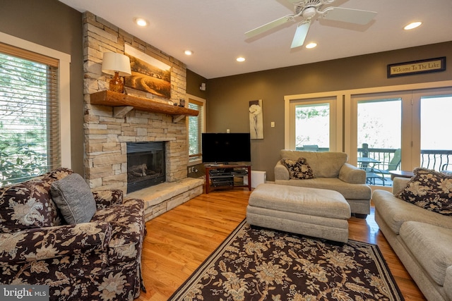 living room featuring a wealth of natural light, ceiling fan, light wood-type flooring, and a stone fireplace