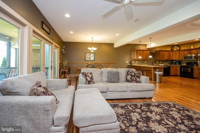 living room featuring ceiling fan with notable chandelier, light hardwood / wood-style floors, and beamed ceiling