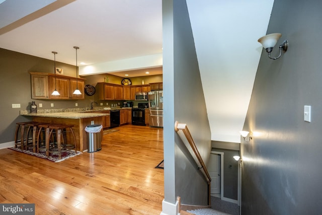 kitchen featuring light stone counters, a kitchen bar, light hardwood / wood-style floors, hanging light fixtures, and stainless steel appliances