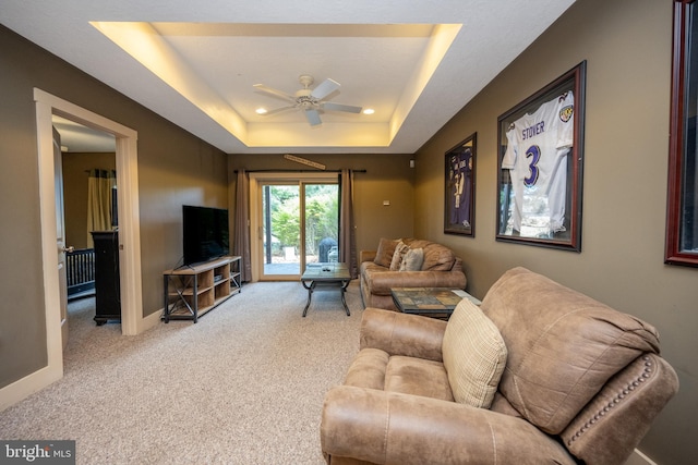 carpeted living room with ceiling fan and a tray ceiling