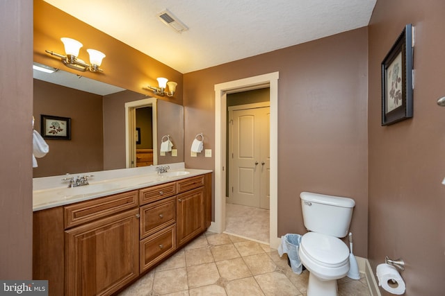 bathroom with vanity with extensive cabinet space, a textured ceiling, dual sinks, toilet, and tile floors