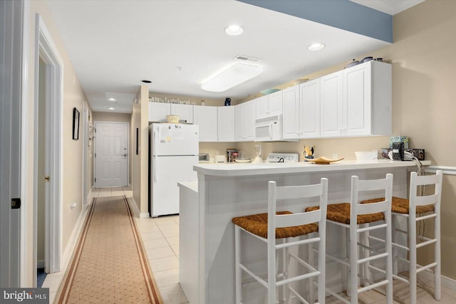 kitchen with kitchen peninsula, white appliances, a kitchen breakfast bar, and white cabinets