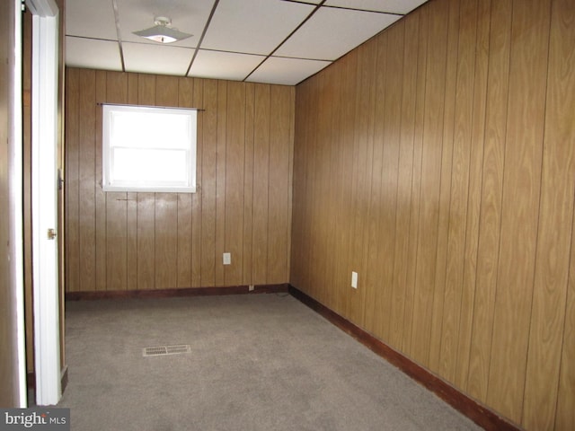 empty room featuring a paneled ceiling, wood walls, and light carpet