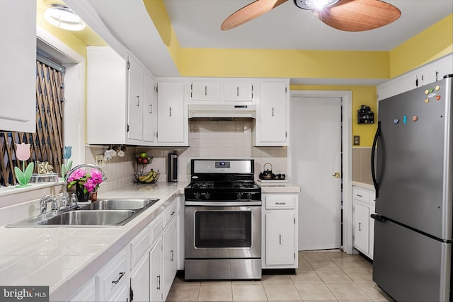 kitchen with ceiling fan, stainless steel appliances, light tile floors, wall chimney range hood, and white cabinetry