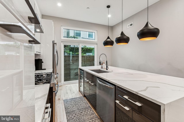 kitchen with decorative light fixtures, stainless steel appliances, wall chimney range hood, a kitchen island with sink, and sink