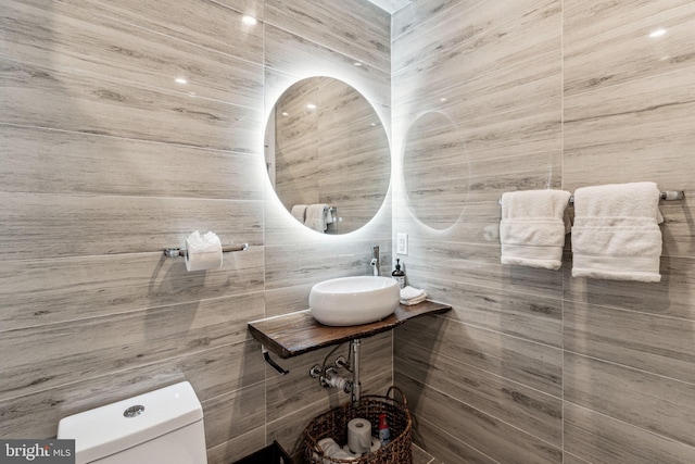 bathroom featuring toilet, tile walls, and sink