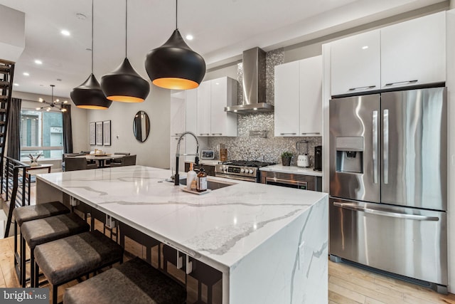 kitchen with light hardwood / wood-style flooring, appliances with stainless steel finishes, wall chimney range hood, tasteful backsplash, and an island with sink