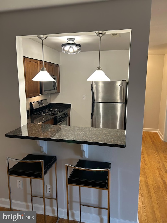 kitchen featuring light hardwood / wood-style flooring, dark stone counters, decorative light fixtures, a breakfast bar area, and appliances with stainless steel finishes