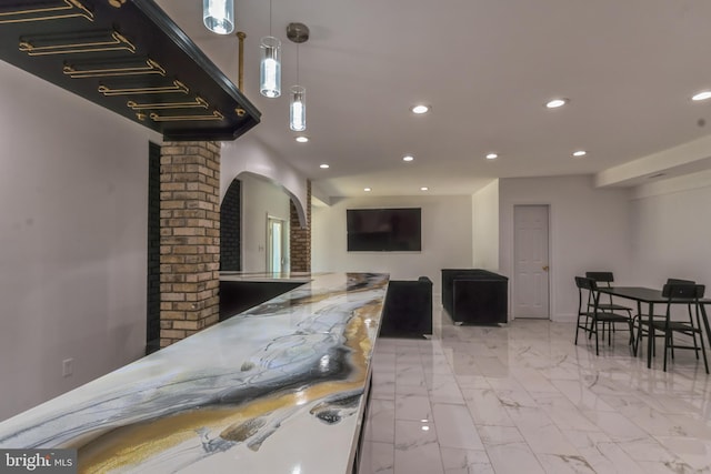 interior space with light stone counters, light tile floors, hanging light fixtures, brick wall, and ornate columns