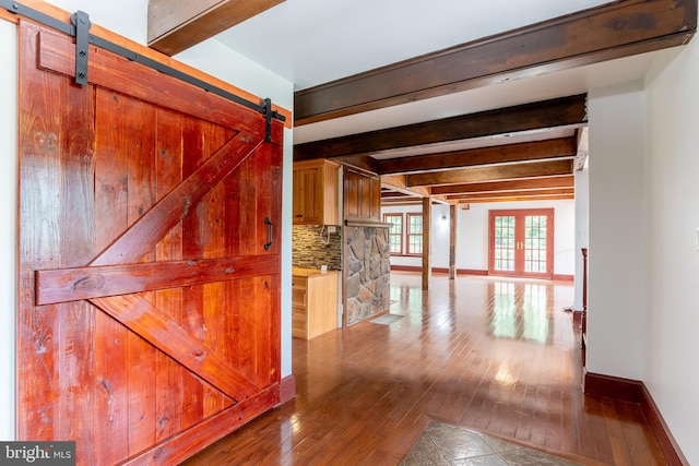 hallway with a barn door, wood-type flooring, and beamed ceiling