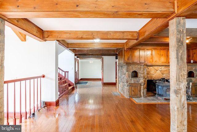 unfurnished living room with beam ceiling, a wood stove, and hardwood / wood-style flooring