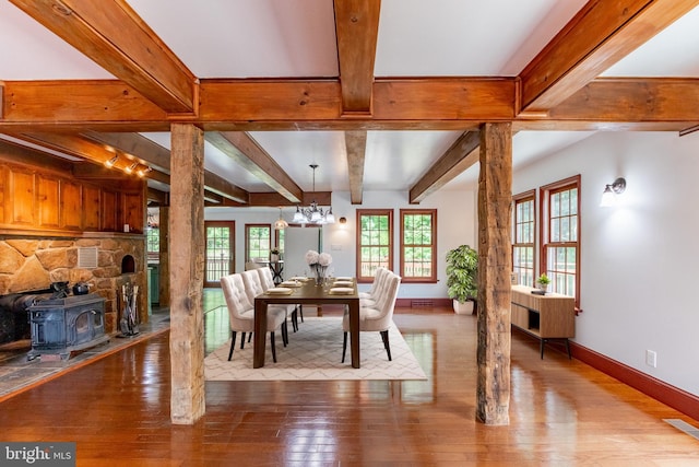 dining space with a notable chandelier, beam ceiling, hardwood / wood-style flooring, a wood stove, and rail lighting