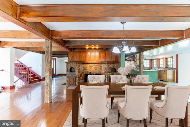 dining area with a notable chandelier, a fireplace, light hardwood / wood-style flooring, and beamed ceiling