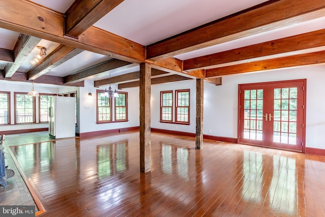 unfurnished living room featuring hardwood / wood-style flooring, a chandelier, beamed ceiling, and french doors