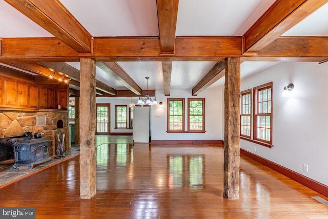 unfurnished living room with hardwood / wood-style floors, beam ceiling, an inviting chandelier, a wood stove, and rail lighting