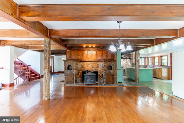 unfurnished living room featuring a notable chandelier, a wood stove, hardwood / wood-style flooring, and beamed ceiling