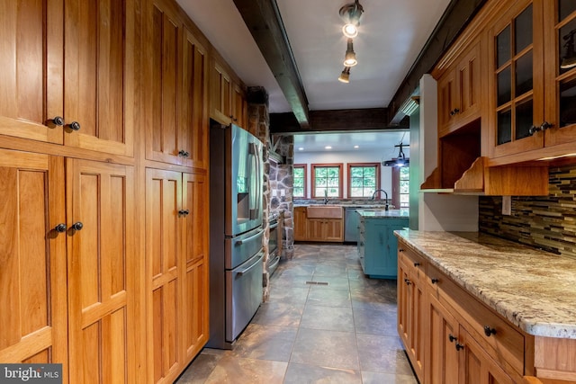 kitchen featuring backsplash, sink, light stone countertops, appliances with stainless steel finishes, and rail lighting