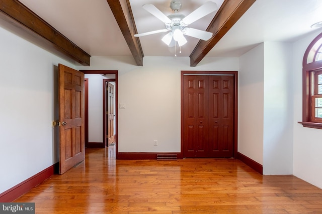 unfurnished bedroom featuring ceiling fan, a closet, light hardwood / wood-style flooring, and beamed ceiling