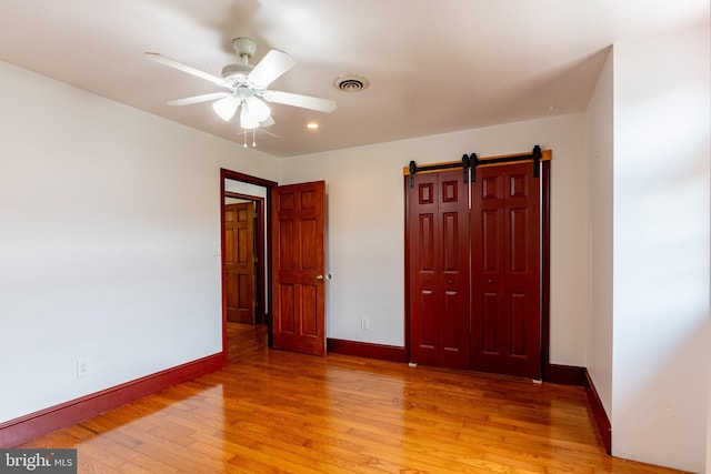 unfurnished bedroom with ceiling fan, a barn door, and light hardwood / wood-style flooring