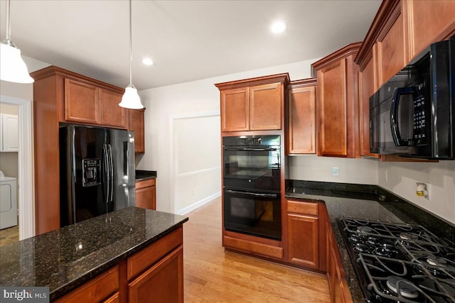 kitchen with dark stone counters, light hardwood / wood-style floors, washer / clothes dryer, hanging light fixtures, and black appliances