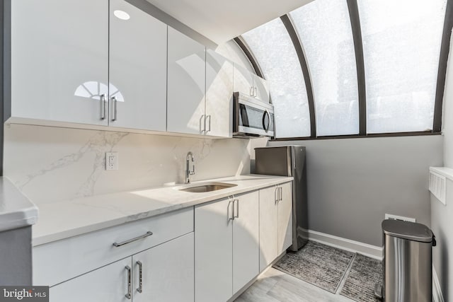 kitchen featuring tasteful backsplash, light stone countertops, sink, and white cabinetry