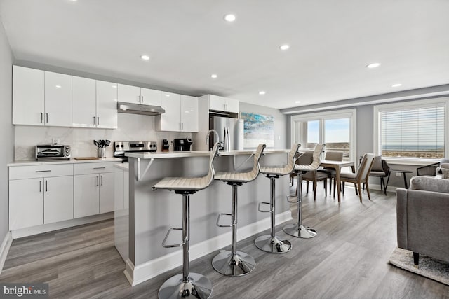 kitchen featuring a kitchen bar, light hardwood / wood-style floors, white cabinets, and stainless steel appliances