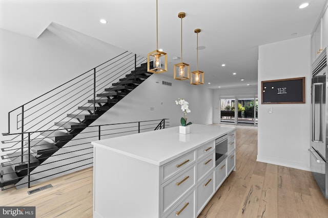 kitchen with hanging light fixtures, light hardwood / wood-style flooring, a center island, and white cabinetry