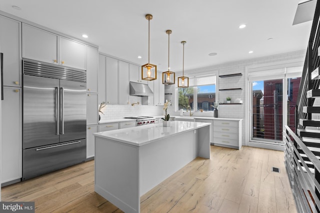 kitchen featuring a kitchen island, light hardwood / wood-style floors, tasteful backsplash, built in refrigerator, and decorative light fixtures