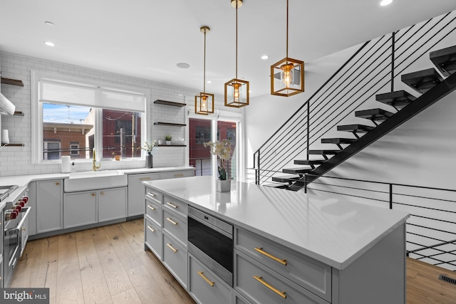 kitchen featuring decorative light fixtures, light hardwood / wood-style flooring, gray cabinets, tasteful backsplash, and a center island