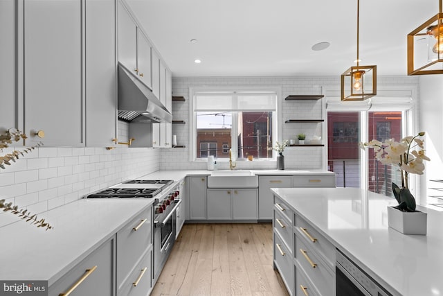 kitchen with premium range, tasteful backsplash, gray cabinetry, pendant lighting, and light wood-type flooring