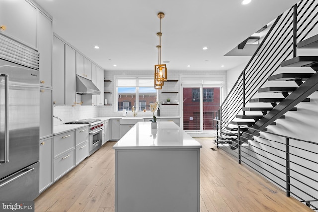 kitchen featuring decorative light fixtures, high end appliances, tasteful backsplash, a center island, and light wood-type flooring