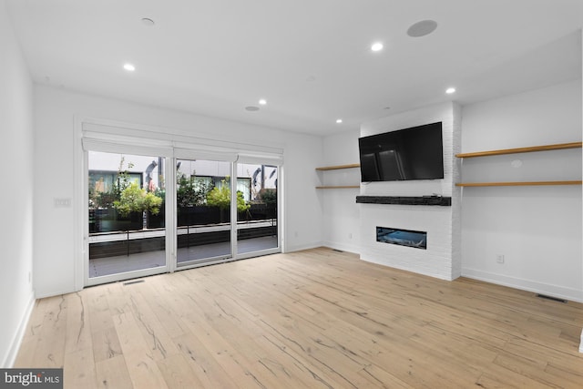 unfurnished living room featuring brick wall, light hardwood / wood-style floors, and a fireplace