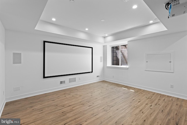 cinema room with light hardwood / wood-style floors and a tray ceiling