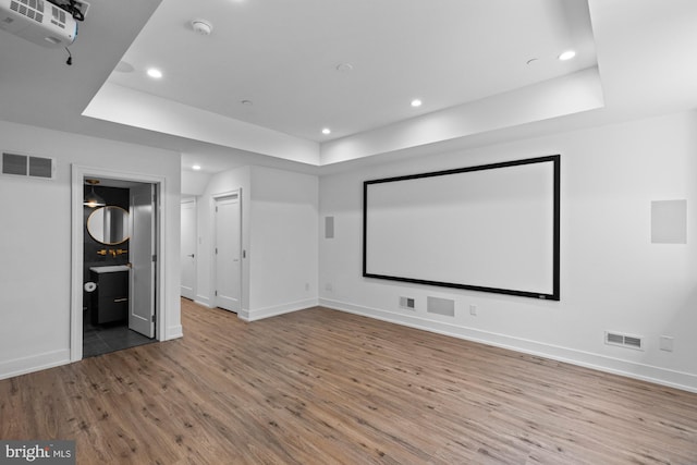 home theater room with light wood-type flooring and a tray ceiling