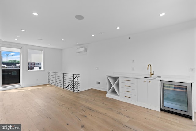 bar featuring light hardwood / wood-style flooring, wine cooler, a wall unit AC, white cabinets, and sink