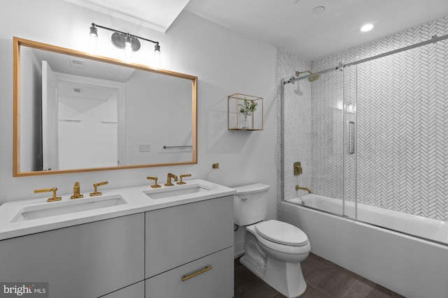 full bathroom with dual sinks, oversized vanity, toilet, and bath / shower combo with glass door