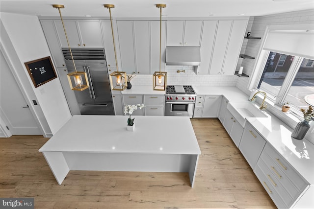 kitchen featuring high quality appliances, pendant lighting, backsplash, and light wood-type flooring