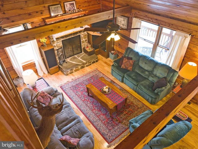 living room featuring vaulted ceiling, light hardwood / wood-style floors, ceiling fan, and a stone fireplace