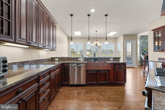 kitchen featuring pendant lighting, dark stone counters, a skylight, stainless steel dishwasher, and dark hardwood / wood-style flooring