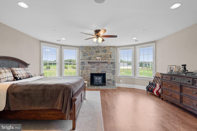 bedroom featuring multiple windows, ceiling fan, light hardwood / wood-style floors, and a wood stove