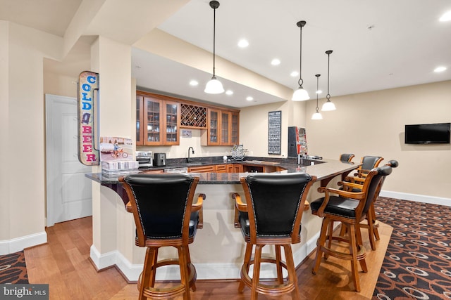 kitchen with a breakfast bar, hanging light fixtures, dark stone countertops, light wood-type flooring, and kitchen peninsula