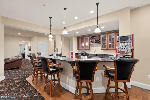 bar with sink, dark stone countertops, hanging light fixtures, and dark wood-type flooring