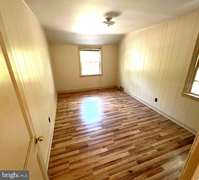 unfurnished room featuring hardwood / wood-style flooring, wood walls, and lofted ceiling