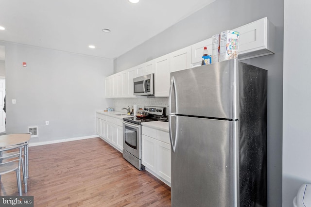 kitchen featuring white cabinets, appliances with stainless steel finishes, backsplash, and light hardwood / wood-style flooring