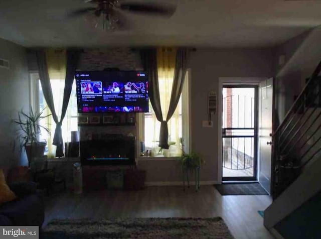 living room featuring a stone fireplace, ceiling fan, and wood-type flooring