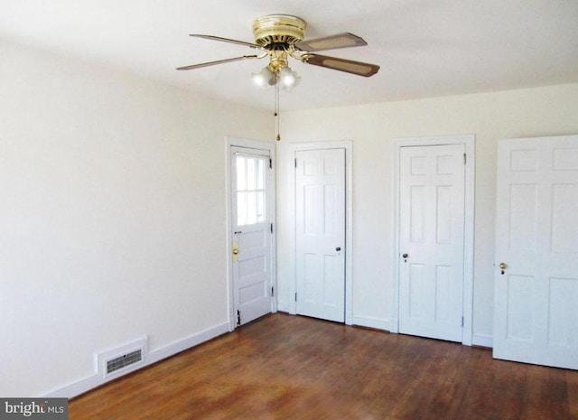 unfurnished bedroom featuring two closets, dark hardwood / wood-style floors, and ceiling fan