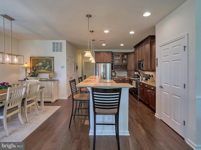 kitchen featuring decorative light fixtures, dark hardwood / wood-style flooring, appliances with stainless steel finishes, a center island with sink, and light stone counters