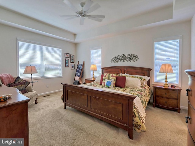 bedroom with light colored carpet, ceiling fan, and a tray ceiling